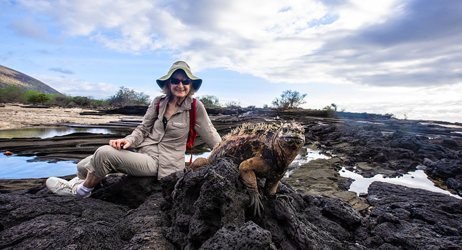 Senior Traveler posing with a Galapagos land Iguana in Santiago Island