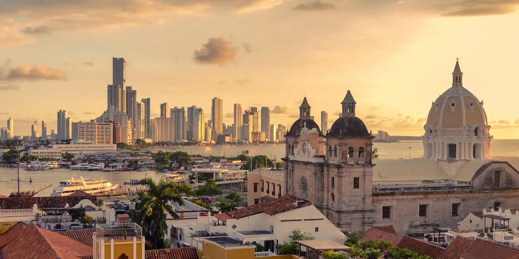 Sunset view of Cartagena’s historic center with cathedral domes in the foreground and the modern skyline in the background.